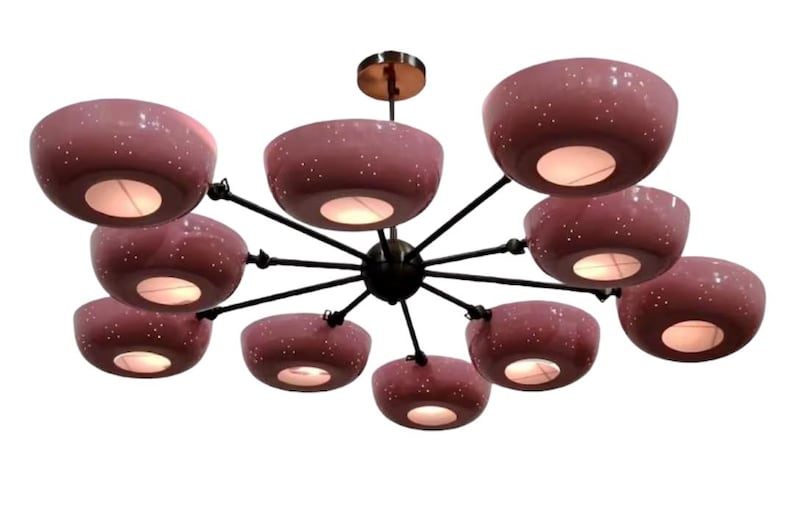 May include: A modern chandelier with ten dusty rose-colored, bowl-shaped shades. Each shade has a speckled pattern and emits a warm light. The fixture has a black frame and a brass-colored ceiling mount.