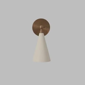 May include: A contemporary wall sconce with a conical, cream-coloured shade and a circular, brass-toned backplate. This indoor lighting fixture has a minimalist design and is suitable for various interior styles.