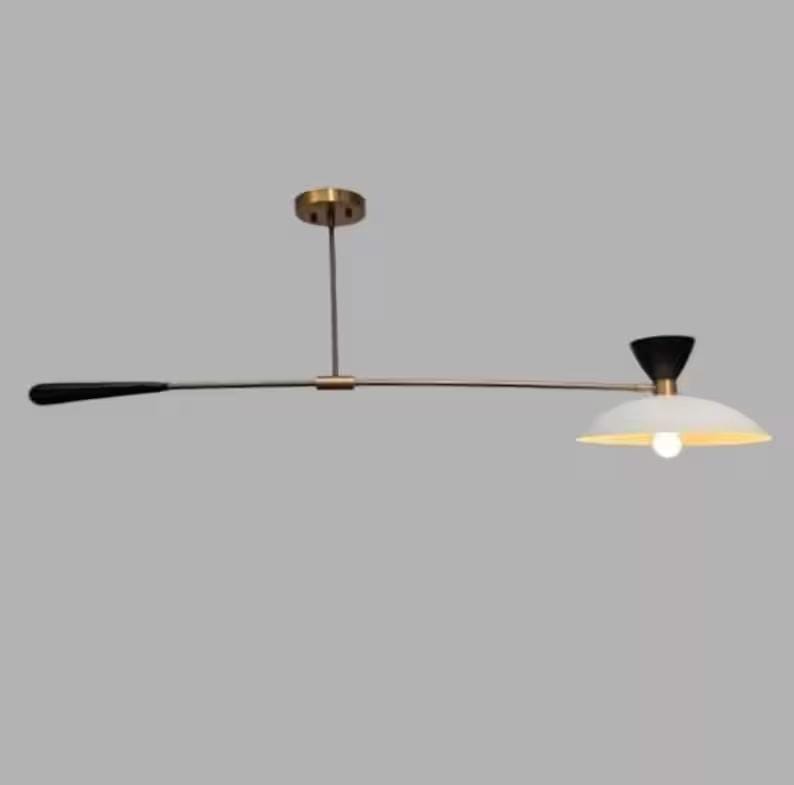 May include: A modern, minimalist ceiling light fixture. It features a long, horizontal bar with a black handle on one end and a white, bowl-shaped shade with a light bulb on the other. The fixture has brass-colored accents.