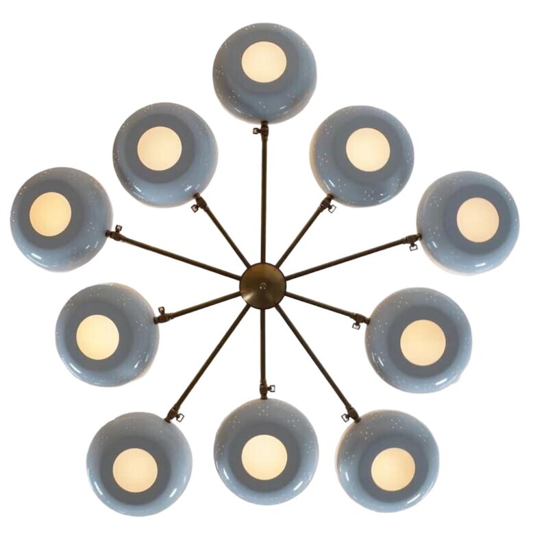 May include: A modern chandelier with a starburst design. It features ten light blue, circular shades with white interiors, each emitting a warm glow. The shades are connected to a central brass fixture by dark metal rods, creating a stylish lighting fixture.