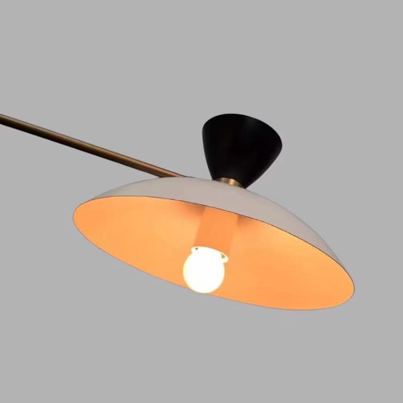 May include: A modern, mid-century style pendant light fixture. The light features a white, saucer-shaped shade with a warm orange interior, a black conical top, and a brass-colored arm. The light bulb is visible.