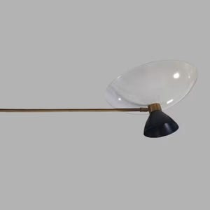 May include: A modern, mid-century style lamp with a clear, oval-shaped shade and a black, cone-shaped light fixture. The lamp has a brass-colored arm and a black base. The design is minimalist and elegant.