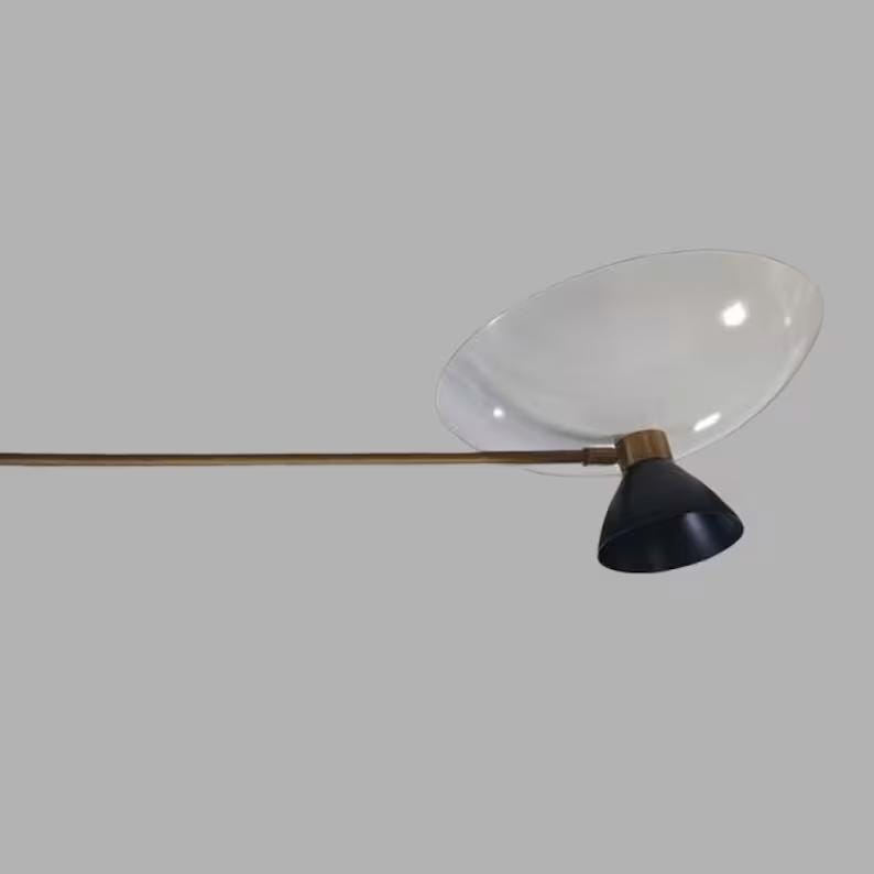 May include: A modern, mid-century style lamp with a clear, oval-shaped shade and a black, cone-shaped light fixture. The lamp has a brass-colored arm and a black base. The design is minimalist and elegant.