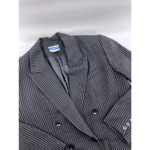 May include: A gray pinstripe blazer with a double-breasted design. The blazer features a notched lapel, multiple buttons, and a label that reads "Pendleton". The jacket is made of a textured fabric.