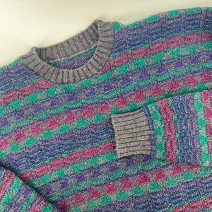 May include: A multi-colored sweater with a crew neck and long sleeves. The sweater features a pattern of horizontal stripes in shades of blue, green, pink, and purple. The collar and cuffs are a solid gray color.
