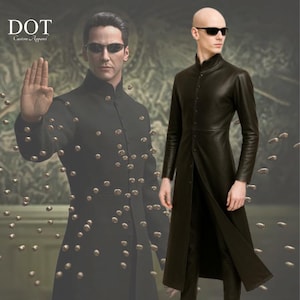 May include: Black long coat with a high collar and button-up front. The coat is worn with black sunglasses. The image also shows a second person wearing a similar coat. The logo "DOT Custom Apparel" is in the top left corner.