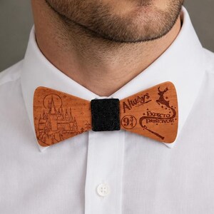 Peut inclure: Nœud papillon en bois marron avec un centre noir. Il présente des gravures avec les mots "Always" et "Expecto Patronum", un château, un cerf et une baguette magique. Porté sur une chemise blanche.