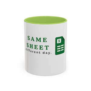 Pode incluir: Uma caneca de cerâmica branca com interior verde-limão. O exterior apresenta o texto verde "SAME SHEET different day." e um ícone verde que se assemelha a um arquivo de planilha com um símbolo "X" impresso na lateral do recipiente.