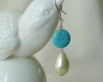 Op de afbeelding: Turquoise en witte hangende oorbellen met een ronde turquoise steen en een parelmoer druppel.
