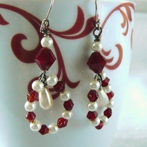 May include: A pair of dangle earrings with a red and white color scheme. The earrings feature a large red crystal bead, a white pearl, and smaller red and white beads.