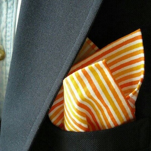 Könnte beinhalten: Ein gestreiftes Einstecktuch in Orange und Weiß. Das Einstecktuch ist gefaltet und in der Tasche eines dunklen Anzugsjackets platziert.