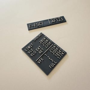 May include: Two rectangular black placards with white engraved text. The top placard displays F-FSCT and SELCALCODE AF123. The bottom square placard lists aviation speed limits including VLE 280KT, VLO EXT 250KT, VLO RET 220KT, and VFE settings 1 215KT, 2 200KT, 3 185KT, and FULL 177KT.