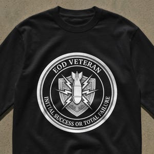 Puede incluir: Camiseta negra de manga larga con un diseño gráfico en blanco y gris. El diseño es un círculo con el texto "EOD Veteran" y "Initial Success or Total Failure" alrededor de una bomba y un escudo.