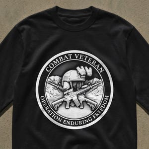 May include: Black long-sleeve shirt featuring a circular graphic with the words "Combat Veteran" and "Operation Enduring Freedom." The graphic includes a helmet, crossed rifles, and binoculars. The design is in shades of gray and white.