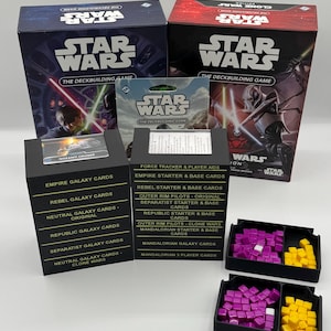 K&ouml;nnte beinhalten: Eine Sammlung von Star Wars Deckbuilding-Spielboxen und Kartensets. Die Boxen sind schwarz und rot mit Star Wars-Branding. Die Kartensets enthalten verschiedene Galaxy-Karten, Starterkarten und Spielerhilfen. Ebenfalls enthalten sind schwarze Tabletts mit lila und gelben Spielsteinen.