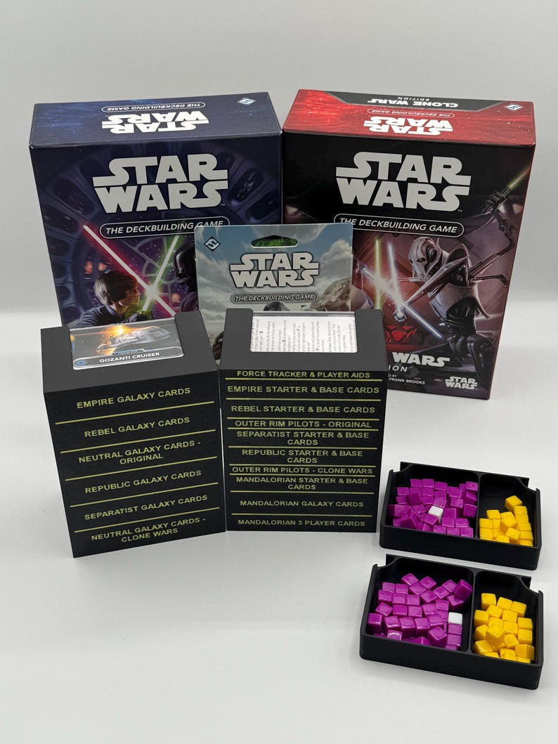 K&ouml;nnte beinhalten: Eine Sammlung von Star Wars Deckbuilding-Spielboxen und Kartensets. Die Boxen sind schwarz und rot mit Star Wars-Branding. Die Kartensets enthalten verschiedene Galaxy-Karten, Starterkarten und Spielerhilfen. Ebenfalls enthalten sind schwarze Tabletts mit lila und gelben Spielsteinen.