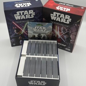 K&ouml;nnte beinhalten: Eine Sammlung von Star Wars Deckbuilding-Spielen. Die Schachteln sind marineblau und rot, mit dem Star Wars-Logo und Charakterillustrationen. Ein Kartenpack und eine Kartenbox sind ebenfalls zu sehen.