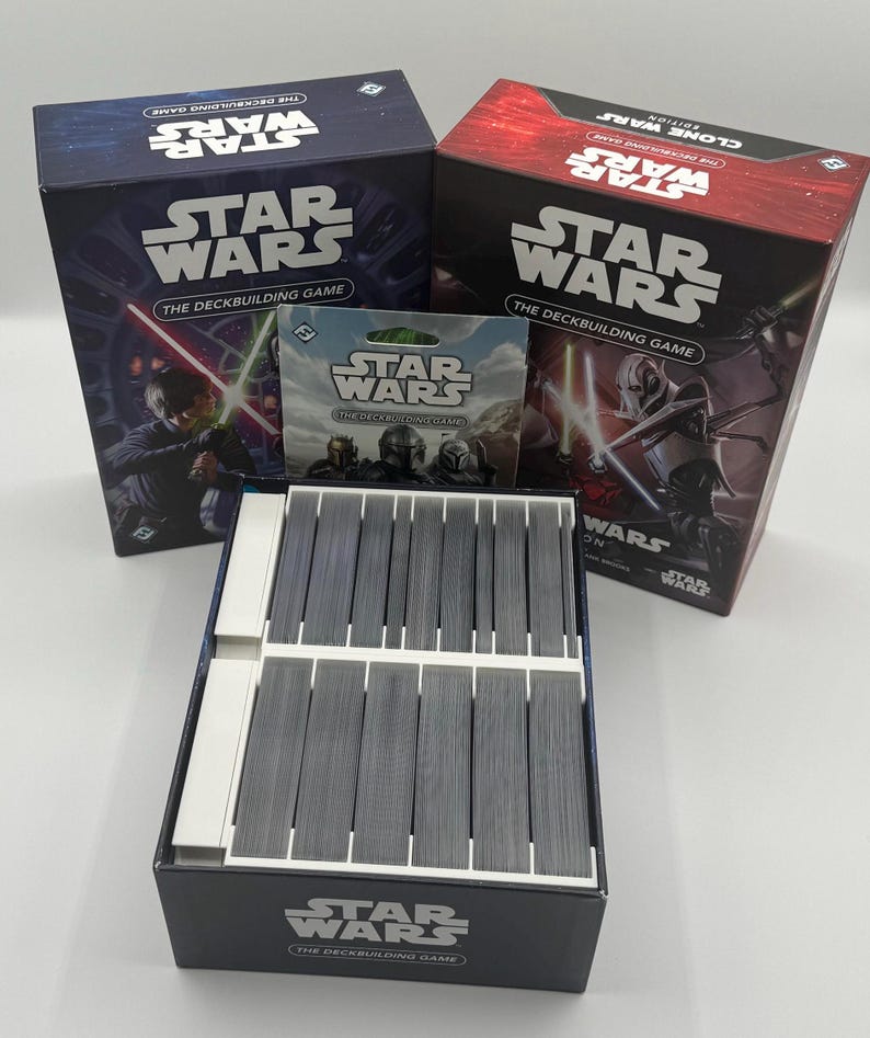 K&ouml;nnte beinhalten: Eine Sammlung von Star Wars Deckbuilding-Spielen. Die Schachteln sind marineblau und rot, mit dem Star Wars-Logo und Charakterillustrationen. Ein Kartenpack und eine Kartenbox sind ebenfalls zu sehen.