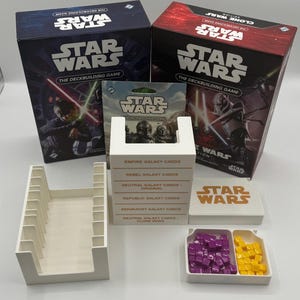 K&ouml;nnte beinhalten: Ein Star Wars Deckbuilding-Spielset. Das Bild zeigt zwei Spielboxen, Kartenhalter, Kartenpakete und Spielsteine. Die Boxen sind marineblau und rot mit Star Wars-Grafiken und Text.