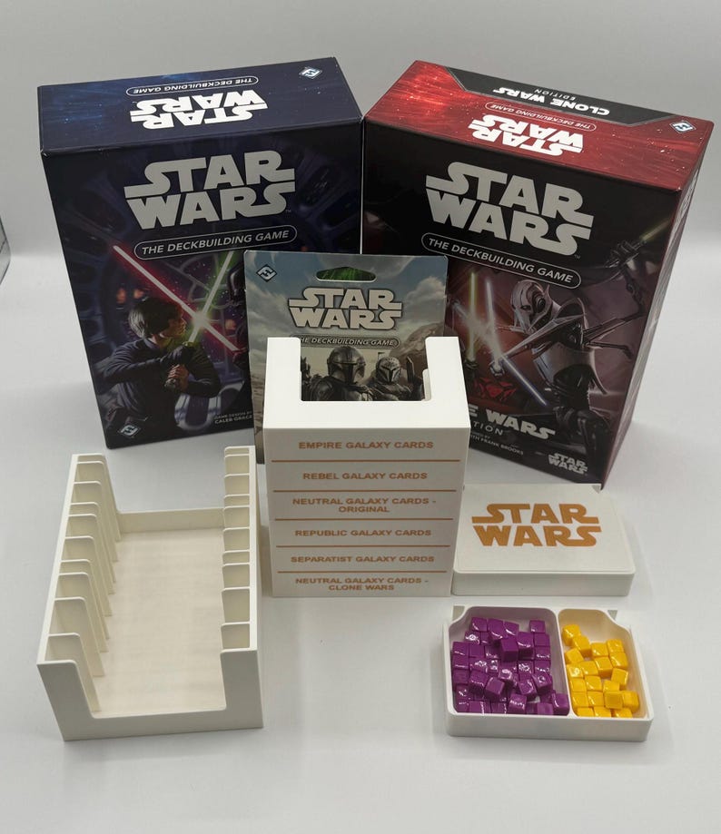 K&ouml;nnte beinhalten: Ein Star Wars Deckbuilding-Spielset. Das Bild zeigt zwei Spielboxen, Kartenhalter, Kartenpakete und Spielsteine. Die Boxen sind marineblau und rot mit Star Wars-Grafiken und Text.