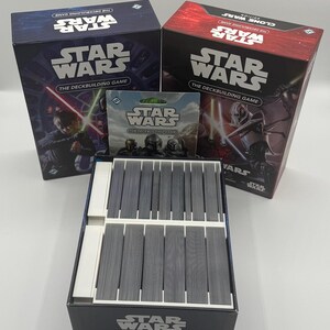 K&ouml;nnte beinhalten: Eine Sammlung von Star Wars Deckbuilding-Spielboxen und -Karten. Die Boxen sind marineblau und rot, mit dem Star Wars-Logo und Charakterillustrationen. Die Spielkarten sind grau und in einer schwarzen Box angeordnet.