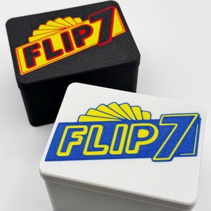 May include: Two small, rectangular boxes with lids. One box is black, the other is white. Both lids feature the text "FLIP 7" in yellow and red or blue, with a stylized sunburst design above the text. The boxes appear to be made of plastic.