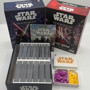 K&ouml;nnte beinhalten: Zwei Star Wars Deckbuilding-Spielboxen, eine blaue und eine rote, mit dem Spieltitel deutlich sichtbar. Die offene Box zeigt einen Kartenorganisator mit grauen Karten sowie Spielsteinen.