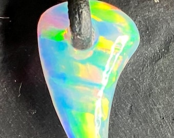 May include: A pear-shaped opal pendant with a rainbow iridescence, suspended from a knotted black leather cord. The gemstone displays a vibrant play of colors, including green, yellow, and blue. The pendant is a unique piece of jewelry.