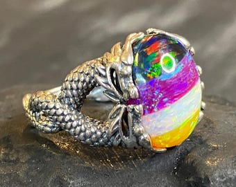 May include: A silver ring featuring a large, colorful opal gemstone. The opal displays vibrant hues of purple, yellow, and green. The ring's band is designed to resemble a dragon's claw, adding a fantasy element.