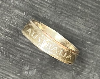 May include: A metallic ring with a smooth, polished finish featuring the word AUSTRALIA embossed in capital letters along the outer band. The ring has a consistent width and a rounded profile, showcasing a reflective surface that catches the light.