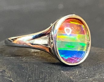 May include: Silver ring with a colorful, rainbow-hued stone. The stone is oval-shaped and features bands of red, orange, yellow, green, blue, and purple. The ring has a simple, elegant design.