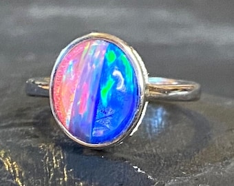 May include: A silver ring featuring an oval-shaped opal. The opal displays a vibrant mix of colors, including pink, blue, and green, creating a striking visual effect. The ring's band is a simple, polished silver.