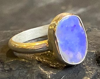 May include: A silver ring with a large, oval-shaped opal gemstone. The opal has a vibrant blue color with hints of purple and is set in a gold-colored bezel. The band is silver.