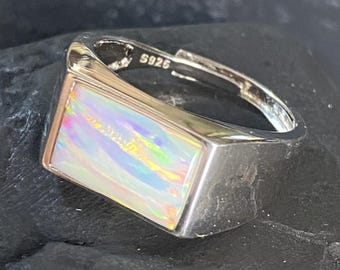 May include: A silver ring with a rectangular opal stone. The opal displays a vibrant play of color, including hues of pink, blue, and yellow. The ring is stamped with "S925".