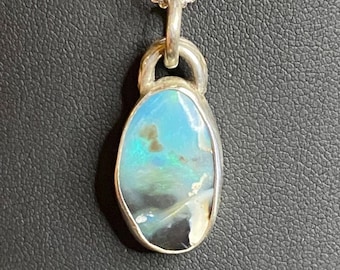 May include: A silver pendant necklace featuring an oval-shaped opal gemstone. The opal displays a mix of blue, green, and black colors. The pendant is suspended from a delicate silver chain, creating a classic and elegant jewelry piece.