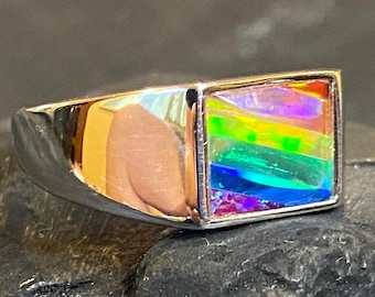 May include: A silver ring with a rectangular, iridescent stone. The stone displays a vibrant spectrum of colors, including red, orange, yellow, green, and blue. The ring has a polished, reflective surface.