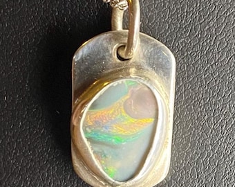 May include: Silver pendant necklace with a rectangular pendant. The pendant features an oval-shaped opal with iridescent colors of green, blue, and yellow. The chain is a delicate silver curb chain.