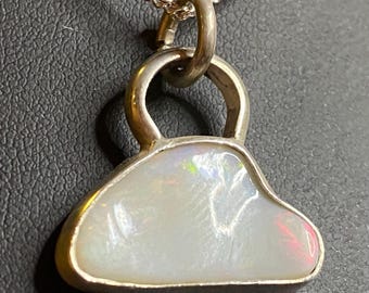 May include: A silver pendant necklace featuring a pear-shaped opal gemstone. The opal has a milky white base with flashes of iridescent color. The pendant is set in a silver bezel and hangs from a delicate silver chain.