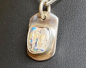 May include: A silver pendant necklace with a rectangular pendant. The pendant has a clear, textured center with iridescent colors. The necklace chain is a small, linked design. The pendant is approximately 1 inch long.