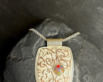 May include: A square silver pendant featuring a textured, raised copper-colored wire pattern and a single round, bezel-set opal gemstone with vibrant flashes of red, orange, and green, suspended from a delicate silver chain.