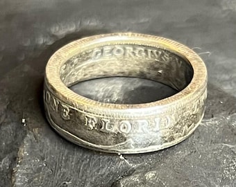 May include: A silver ring with engraved text, including "ONE FLORIDA" and "GEORGIVS". The ring has a worn, vintage appearance. The ring is a band style.