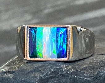 May include: A silver ring with a rectangular opal stone. The opal displays a vibrant array of colors, including blue, green, and white. The ring has a polished finish and a classic design, suitable for everyday wear.