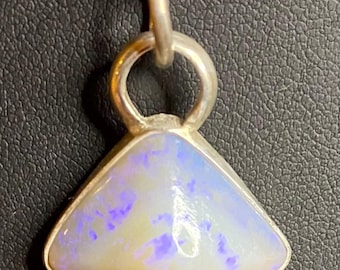 May include: A silver pendant necklace featuring a triangular opal stone. The opal has a white base with purple and blue flecks. The pendant is attached to a silver chain.