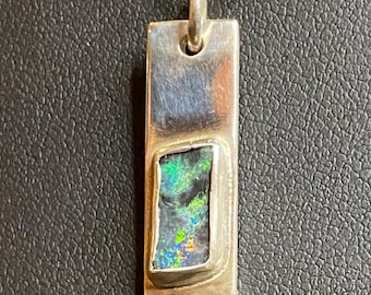 May include: Silver pendant necklace featuring a rectangular pendant with a vibrant, iridescent opal stone. The opal displays a mix of green, blue, and yellow hues. The pendant hangs from a delicate silver chain.