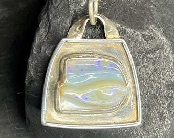 May include: A silver pendant necklace featuring a rectangular pendant with a unique, colorful opal stone. The opal displays shades of blue, yellow, and white. The pendant is suspended from a delicate silver chain, creating an elegant accessory.