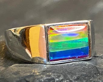May include: A silver ring with a rectangular, iridescent gemstone. The gemstone displays a vibrant rainbow of colors, including red, orange, yellow, green, blue, and purple. The ring has a polished, reflective surface.