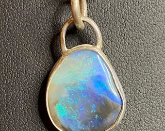 May include: A silver pendant necklace featuring a teardrop-shaped opal. The opal displays a vibrant play of color with blues, greens, and hints of purple. The pendant is suspended from a delicate silver chain, creating an elegant accessory.