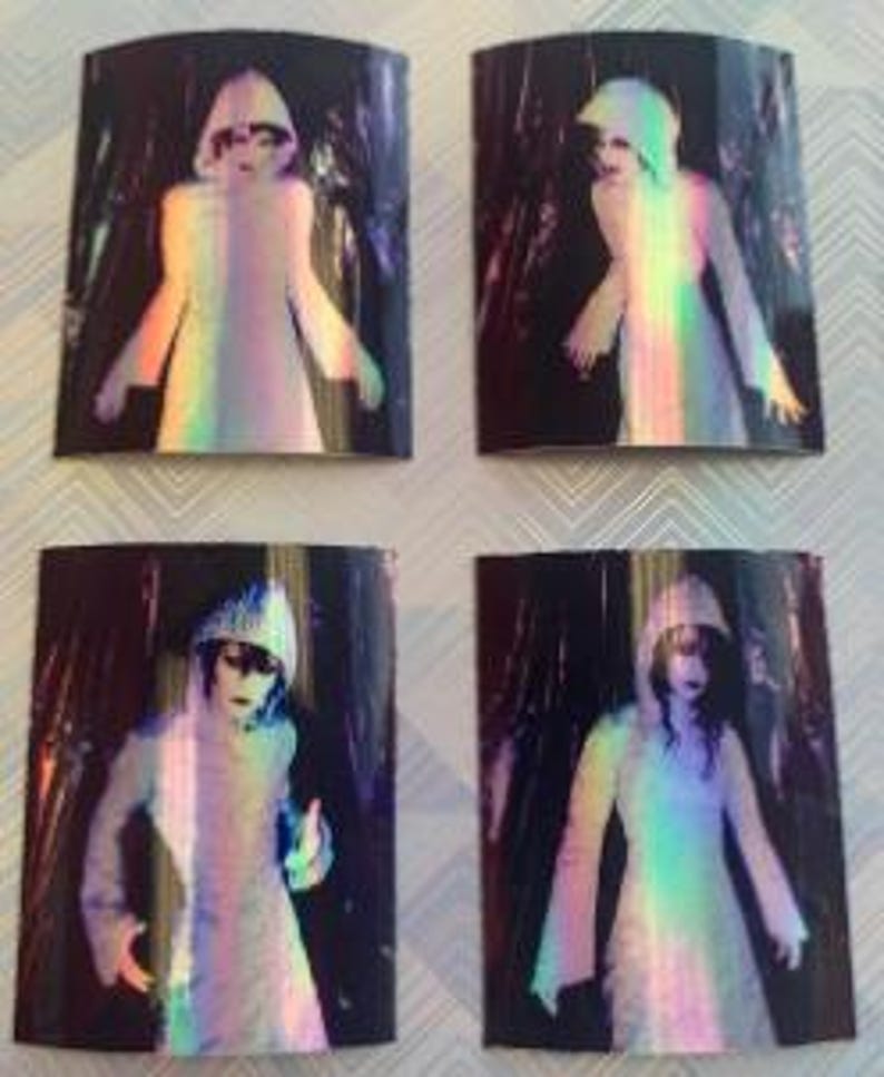 Op de afbeelding: Vier iriserende holografische stickers met een figuur in een witte gewatteerde kap met een donkere achtergrond.