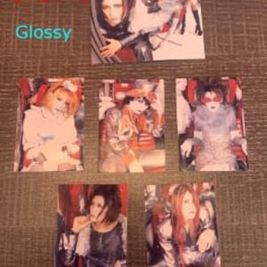 Op de afbeelding: Vijf glanzende fotokaarten met een Japanse rockband, Malice Mizer. De bandleden zijn gekleed in zwart en wit met dramatische make-up. De kaarten zijn bedrukt met de naam van de band, Malice Mizer.