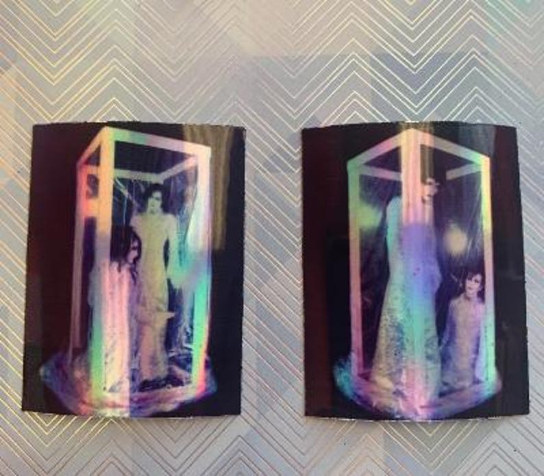 Op de afbeelding: Twee iriserende holografische afbeeldingen van mensen die in een kubusvormig frame staan. De afbeeldingen zijn op een zwarte achtergrond.